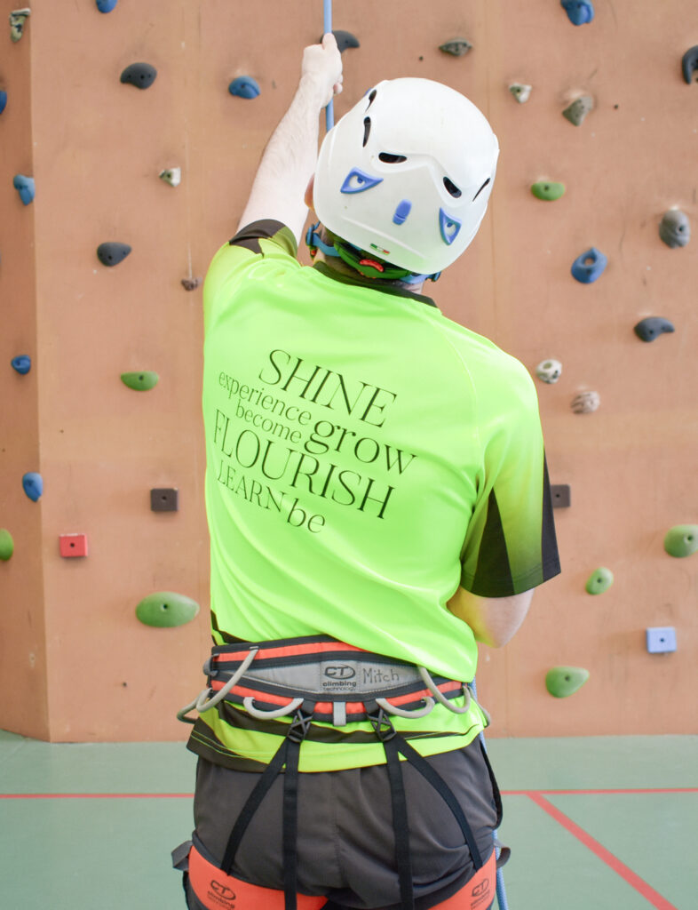Man wearing a helmet, holding a rope during a rock climbing activity at Camp Fairbridge