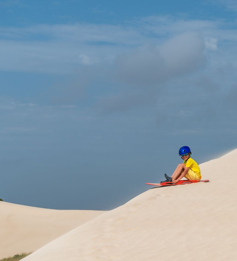 A kid wearing a helmet enjoys sandboarding at South Gates beach, Geraldton Fairbridge Camp