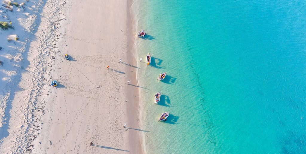 Five boats are ready to sail on a stunning beach during a sea trekking activity at Camp Fairbridge