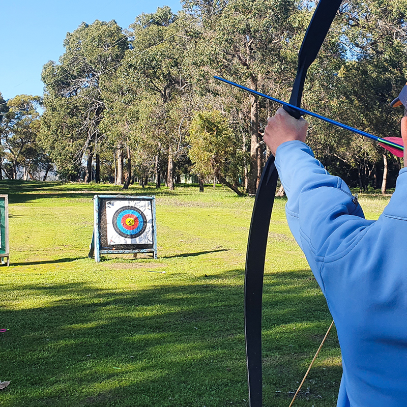 Person aiming a bow and arrow at a target during an archery session at Dampier Camp Fairbridge