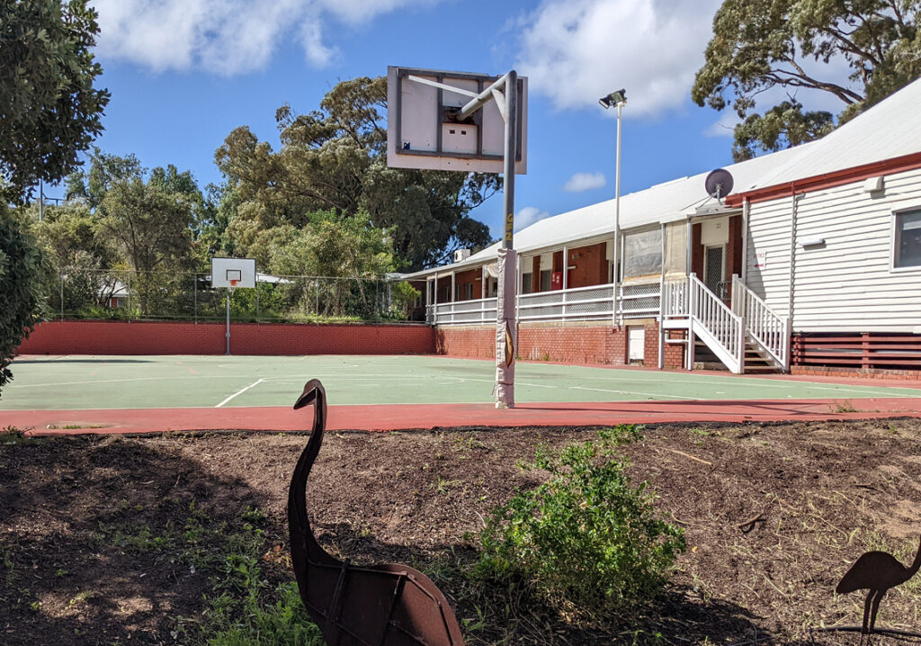 A basketball court with a bird statue stands in front of a house at Geraldton Camp Fairbridge
