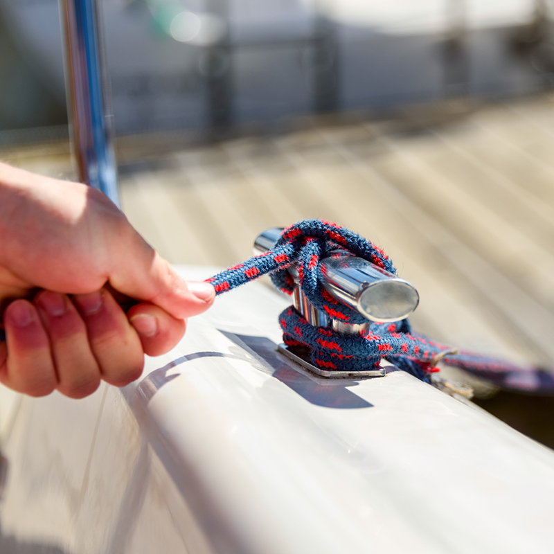 A person tying a boat's rope knot for safety and adjusting the sails while sailing at Camp Bridge beach