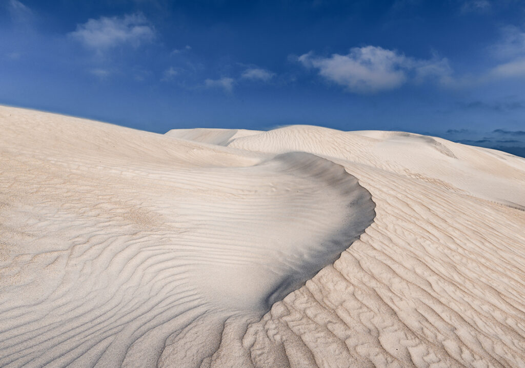 Majestic sand dunes of Camp Fairbridge, set against a clear blue sky, perfect for sandboarding activities