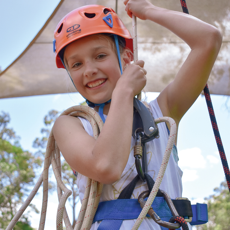 A kid hanging on a rope, wearing a harness and helmet for safety, during a ropes course at Camp Fairbridge
