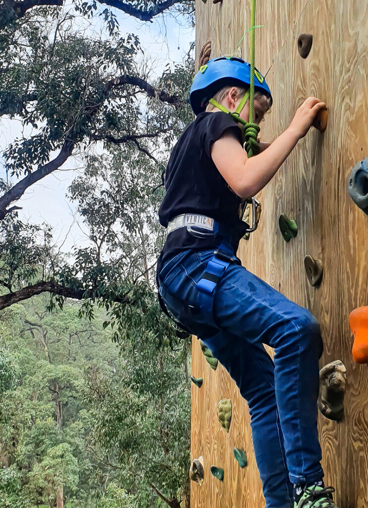 A kid in a helmet and harness enjoys outdoor rock climbing at Camp Fairbridge in Pinjarra