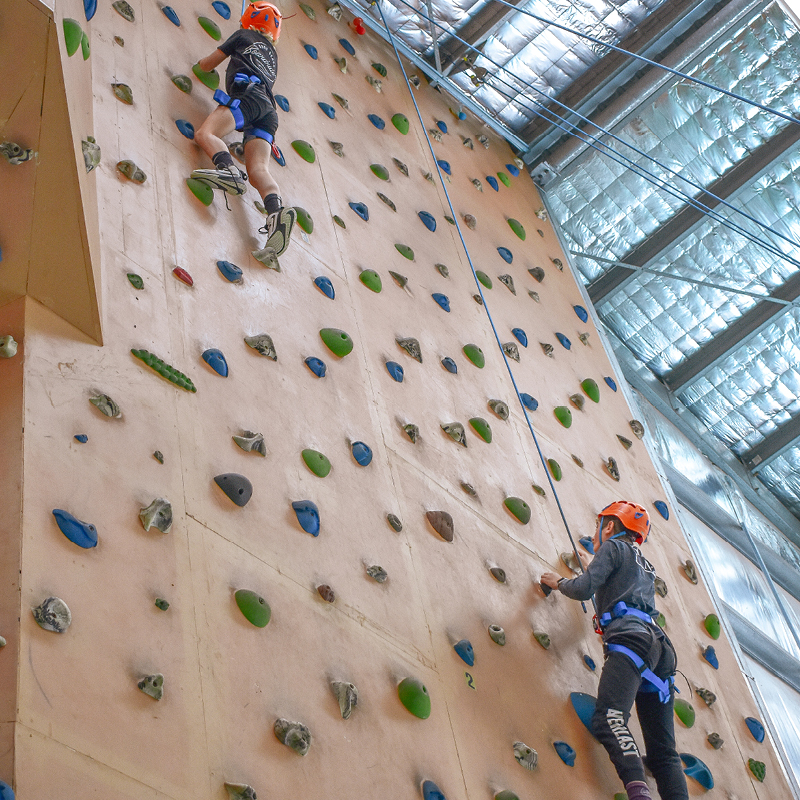 Two kids wearing helmets and harnesses enjoy indoor wall climbing at Point Peron Camp Fairbridge