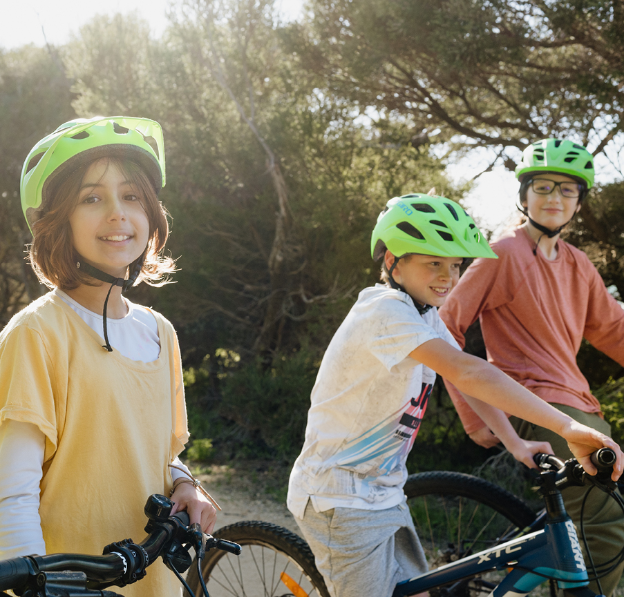 Three kids wearing helmets enjoy cycling at Camp Fairbridge