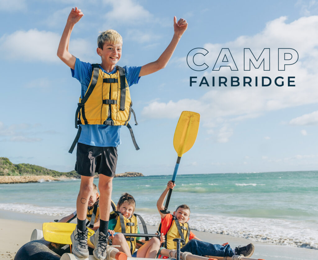 A boy stands joyfully with his team in the background during a kayak activity at Camp Fairbridge