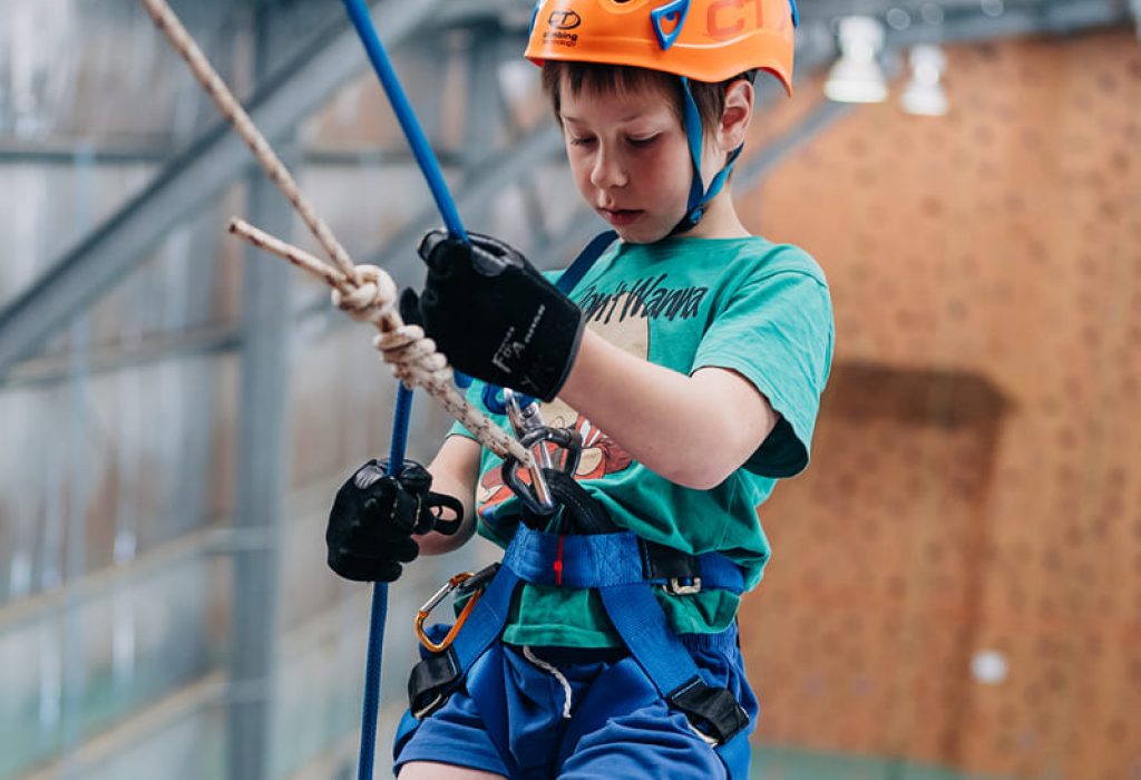 A kid wearing a harness and helmet enjoys rappelling at Point Peron, Camp Fairbridge A kid wearing a harness and helmet enjoys rappelling at Point Peron, Camp Fairbridge